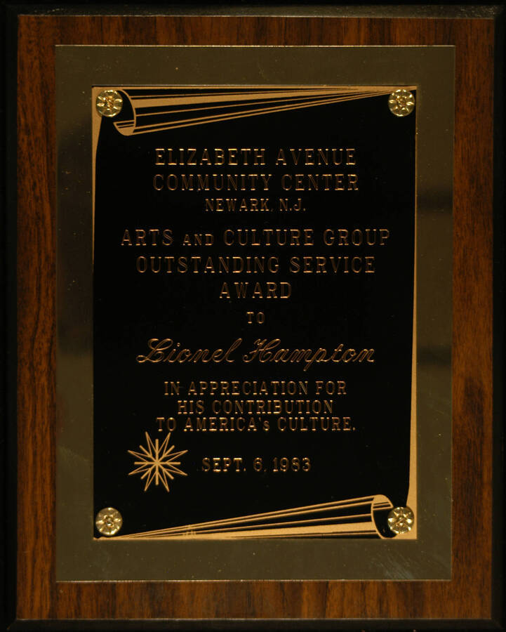 Plaque. 10"x8" Wood finish plaque with engraved double plate Arts and Culture Group Outstanding Service Award presented to Lionel Hampton by the Elizabeth Avenue Community Center in appreciation for his contribution to America's culture. Newark, N.J., Sept. 6, 1983