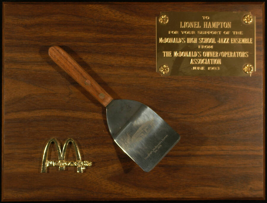 Plaque. 9"x12" Wood finish plaque with McDonald's logo, spatula, and engraved plate To Lionel Hampton from the McDonald's Owner/Operators Association for his support of the McDonald's High School Jazz Ensemble. June 1983