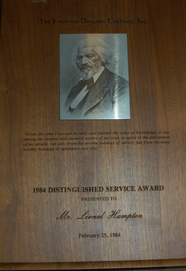 Plaque. 12"x9" Engraved wood finish plaque with picture of Frederick Douglass plate Distinguished Service Award presented to Lionel Hampton by the Frederick Douglass Coalition. Feb. 25, 1984