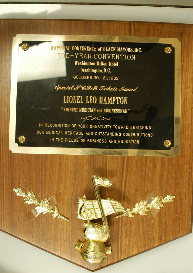 Plaque. 15"x12" Wood finish plaque with musical theme and engraved double plate Special NCBM Tribute Award presented to Lionel Hampton by the National Conference of Black Mayors in recognition of his musical creativity and outstanding contributions in the fields of business and education on the occasion of the Mid-Year Convention at the Washington Hilton Hotel. Washington, D.C. Oct. 20-21, 1982