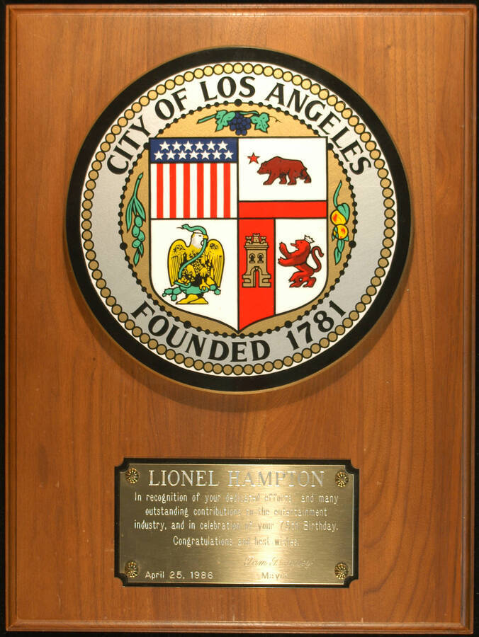Plaque. 16"x12" Wood finish plaque with a 8" color Seal of the  City of Los Angeles and engraved double plate To Lionel Hampton from the City of Los Angeles on the occasion of his 75th birthday. Tom Bradley, Mayor. Los Angeles, CA, Apr. 25, 1986.