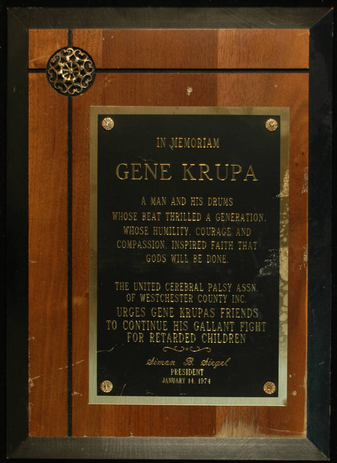 Plaque. 14"x 10" Wood finish plaque, squared on the left upper corner finishing in a rosette, with engraved plate In Memoriam Gene Krupa. The United Cerebral Palsy Association of Westchester County urges Gene Krupa's friends to continue his fight for retarded children. Simon B. Siegel, President. Westchester County, NY, Jan. 14, 1974
