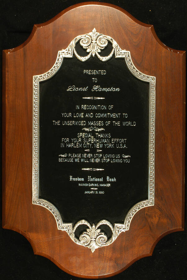 Plaque. 21 1/4"x14" Wood finish plaque with black engraved  plate inside silver casting To Lionel Hampton from Freedom National Bank for his effort in Harlem City. Waymon Darkins, Manager. Harlem, NY, Jan. 31, 1980