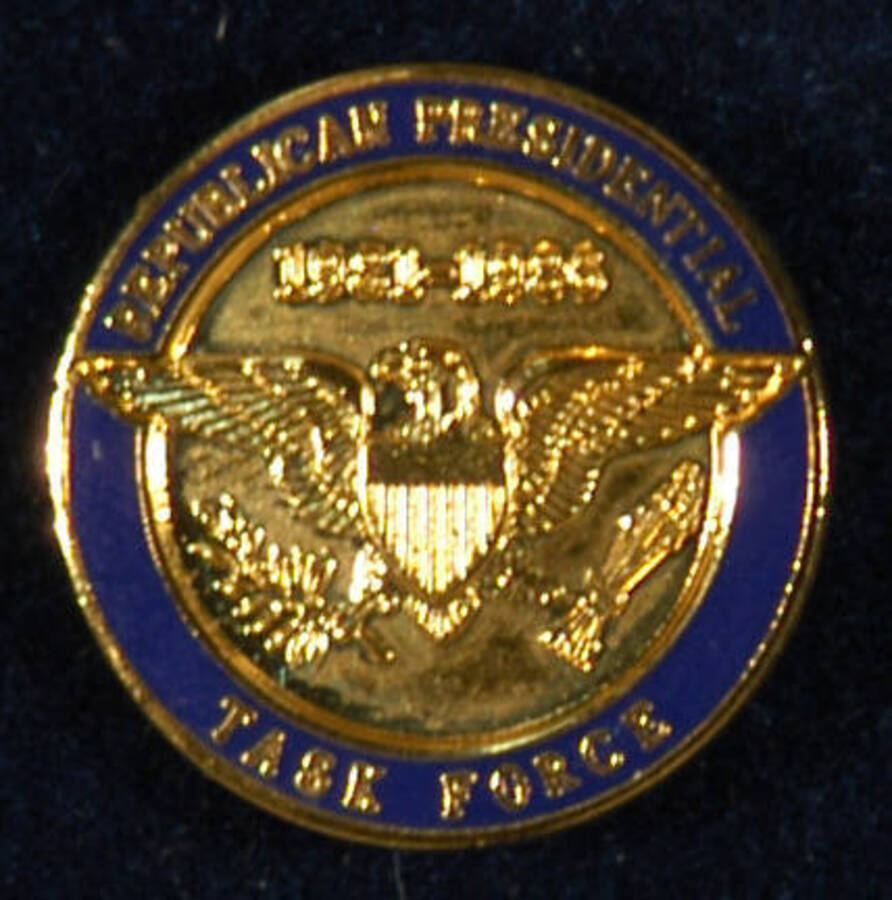 Pin. 3/4" Gold pin depicting a bald eagle with its wings outstretched and the dates "1981-1986" above it. A blue enameled border encircling the pin bears the inscription "Republican Presidential Task Force." It is inside a blue velvet jewelry box