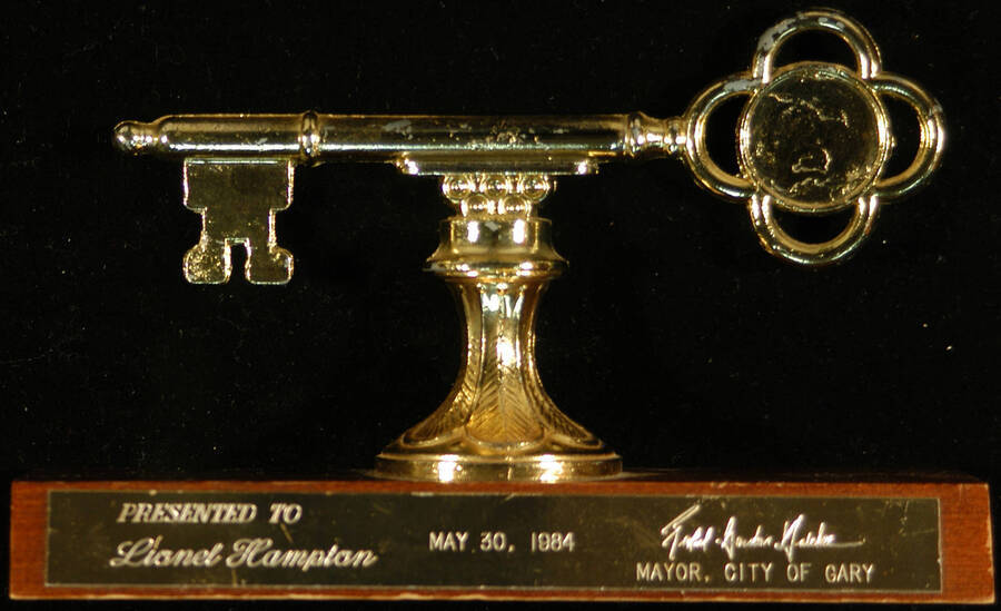 Key to the City. 5 1/2" Gold key on a flower motif base mounted on a 2"x6 1/2" wood plaque with engraved plate Ceremonial key to the City of Gary presented to Lionel Hampton. Richard Gordon Hatcher, Mayor. Gary, IN, May 30, 1984