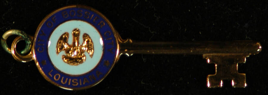 Key to the City.  2" Gold key with the Seal of the Bossier City on one side of the bow. It is inside a 1 1/4"x3" plastic box with clear lid Ceremonial key to the City of Bossier presented to Lionel Hampton. Bossier, LA