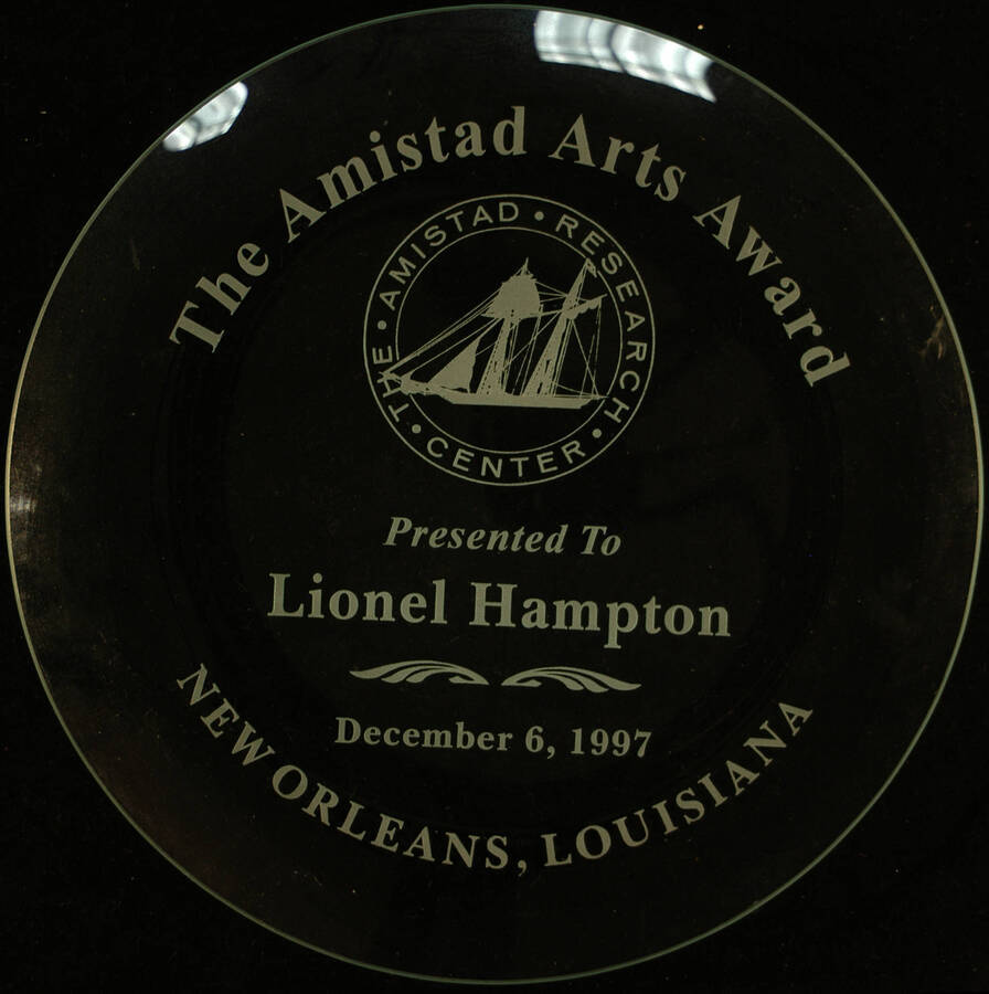 Plate. 12" Clear glass engraved plate and 5"x8" oval solid wood base The Amistad Arts Award presented to Lionel Hampton by the Amistad Research Center. New Orleans, LA, Dec. 6, 1997