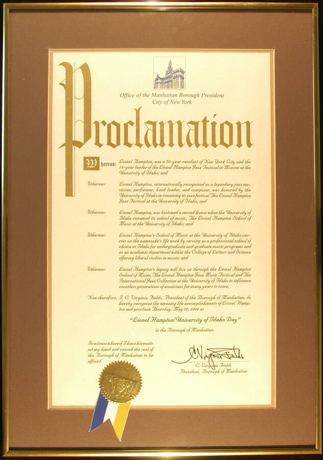Framed Certificate. 22"x16" Gold aluminum frame holding a proclamation with gold foil seal and blue, white, and yellow ribbon in gray mat under glass Borough of Manhattan proclaims May 20, 2004 as Lionel Hampton University of Idaho Day. C. Virginia Fields, President. New York, NY, May, 2004