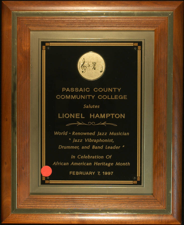 Plaque. 15 1/2"x12 1/2" Wood frame holding a engraved double plate To Lionel Hampton from the Passaic County Community College, in celebration of African American Heritage Month. Feb. 7, 1997