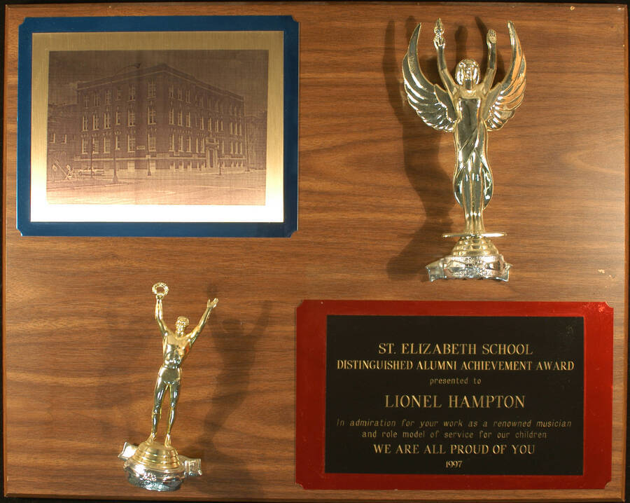 Plaque. 16"x20" Wood finish plaque with two figures and two double engraved plates: one depicting a screen printed picture of a building and the other, a dedication Distinguished Alumni Achievement Award presented to Lionel Hampton by the St. Elizabeth School, in admiration for his work as a musician and role model service for their children. 1997