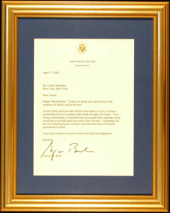 Plaque. 12 1/2"x10" Gold frame holding a letter from George W. Bush to Lionel Hampton, dated from April 17, 2002, in blue mat under glass. The letter is on paper from the White House, Washington, D.C. Letter congratulating Lionel Hampton on his 94th Birthday
