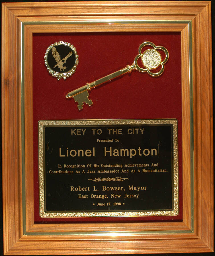 Key to the City Plaque.  18"x15" Wood frame holding a disc, a 8" ceremonial key and a engraved plate on a red velvet background Ceremonial key to the City of East Orange presented to Lionel Hampton. Robert L. Bowser, Mayor. East Orange, NJ, June 17, 1998