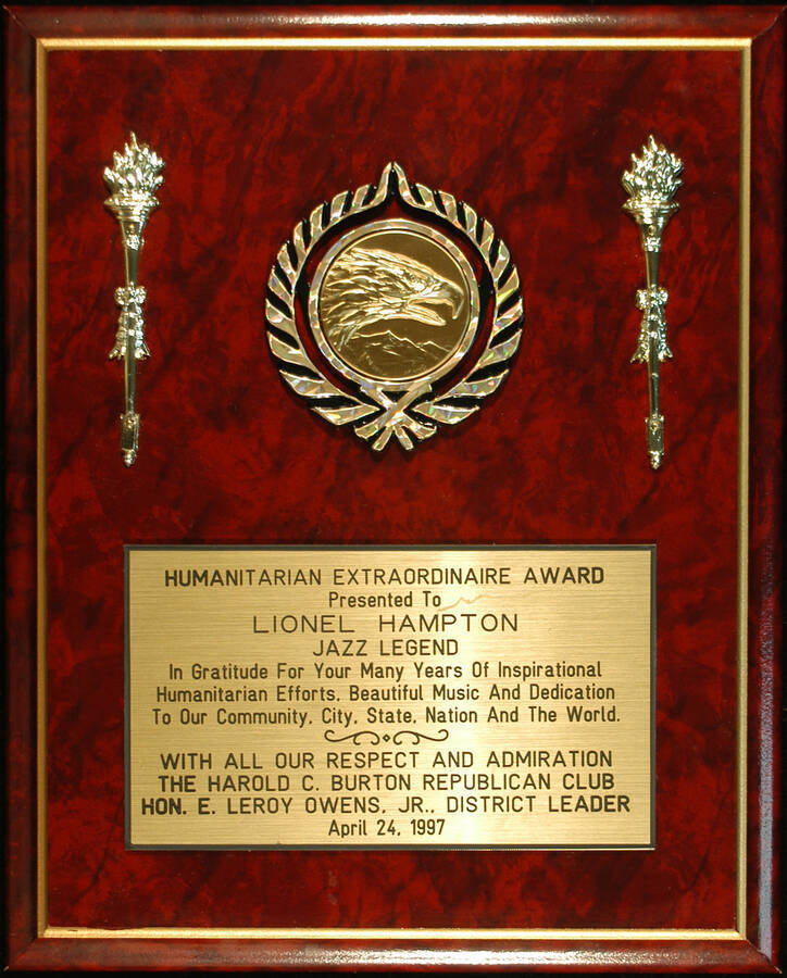 Plaque. 13"x10 1/2" Wood finish plaque with 2" disc inserted in a holder flanked by two torches and engraved plate Humanitarian Extraordinaire Award presented to Lionel Hampton by the Harold C. Burton Republican Club. E. Leroy Owens, Jr., District Leader. Apr. 24, 1997
