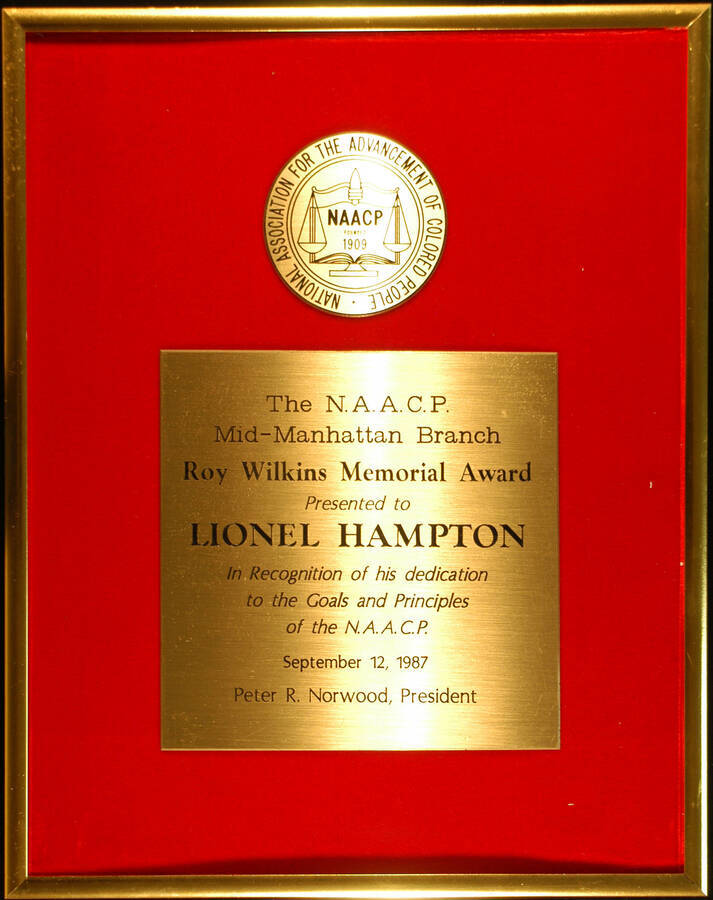 Plaque. 14 1/2"x11 1/2" Aluminum frame holding a disk bearing the logo of the National Association for the Advancement of Colored People-NAACP and engraved plate on red velvet background Roy Wilkins Memorial Award presented to Lionel Hampton by the Mid-Manhattan Branch of the NAACP in recognition of his dedication to the goals and principles of the association. Peter R. Norwood, President. Sep. 12, 1987