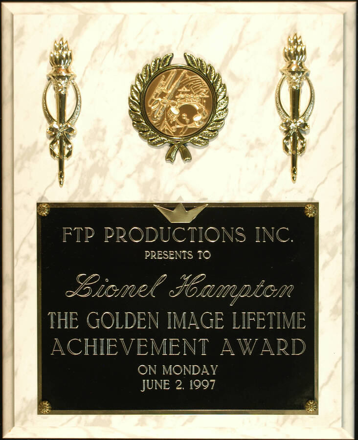 Plaque. 13"x10 1/2" White marbleized wood finish plaque with musical theme disc inserted in a holder flanked by two torches and engraved double plate Golden Image Lifetime Achievement Award presented to Lionel Hampton by [For the People Productions]-FTP Productions. June 2, 1997
