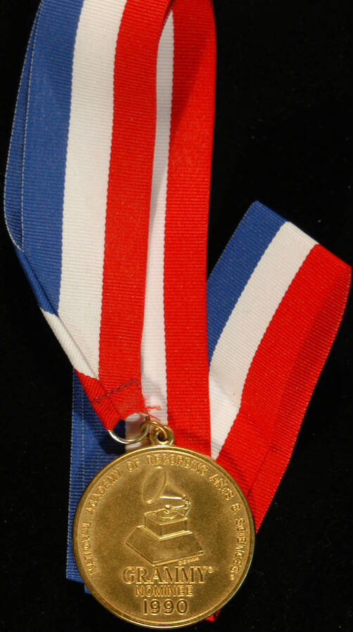 Medal. 2" Gold medal with red, white, and blue neck ribbon. On the obverse, the medal depicts a gramophone and the inscription "National Academy of Recording Arts and Sciences" and "Grammy Nominee 1990." It is inside a plastic box with clear lid