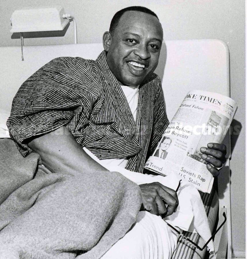 8 1/2 x 6 1/2 inch photograph. Lionel Hampton in bed reading The Roanoke Times newspaper. [Roanoke, VA]