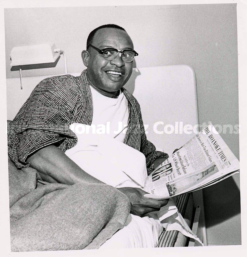 8 1/2 x 6 1/2 inch photograph. Lionel Hampton in bed reading The Roanoke Times newspaper. [Roanoke, VA]