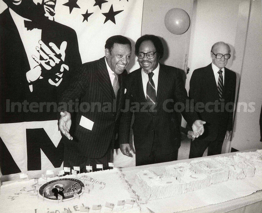 8 x 10 inch photograph. Lionel Hampton poses with Sir Roland Hanna on the occasion of his Birthday party. A plaque on the center of the birthday cake reads: Good Will Ambassador; Lionel Hampton Vibe President