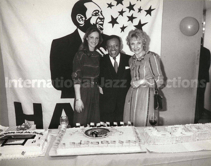 8 x 10 inch photograph. Lionel Hampton poses with two unidentified women on the occasion of his Birthday party. A plaque on the center of the birthday cake reads: Good Will Ambassador; Lionel Hampton Vibe President