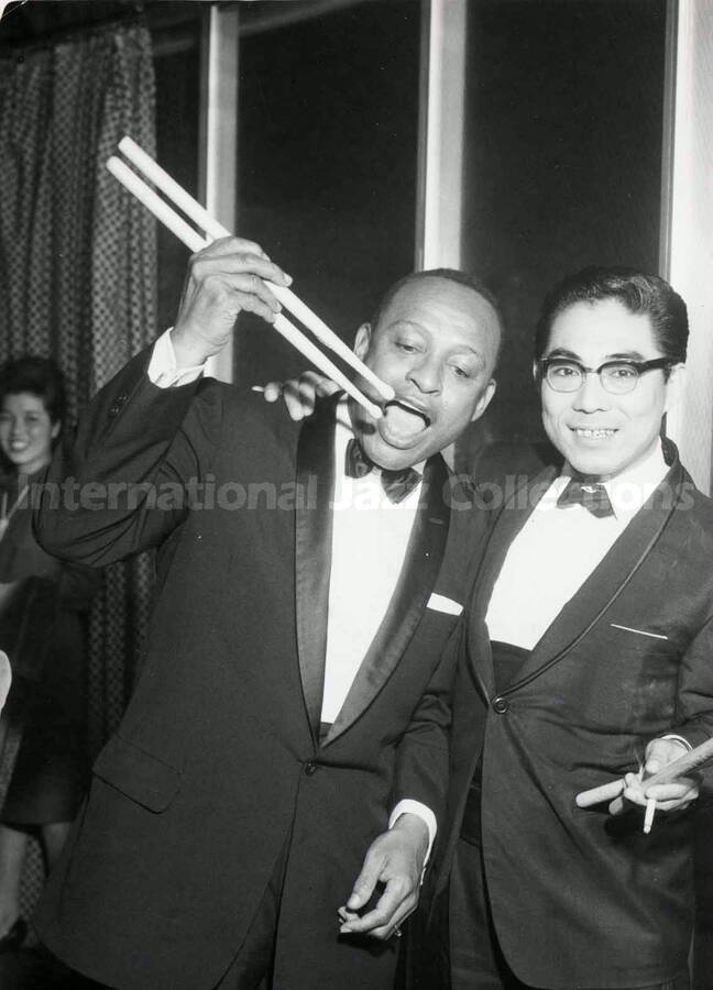 10 x 8 inch photograph. Lionel Hampton poses with unidentified man, pretending that the drumsticks are chopsticks