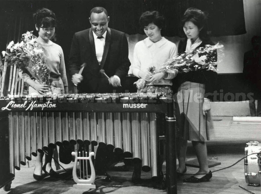 4 1/2 x 6 1/2 inch photograph. Lionel Hampton playing the vibraphone observed by unidentified women [in Japan]