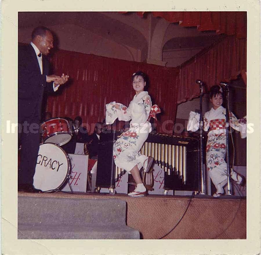 3 1/2 x 3 1/2 inch photograph. Lionel Hampton's band and two unidentified women dressed in Japanese costume, dancing [in Japan]