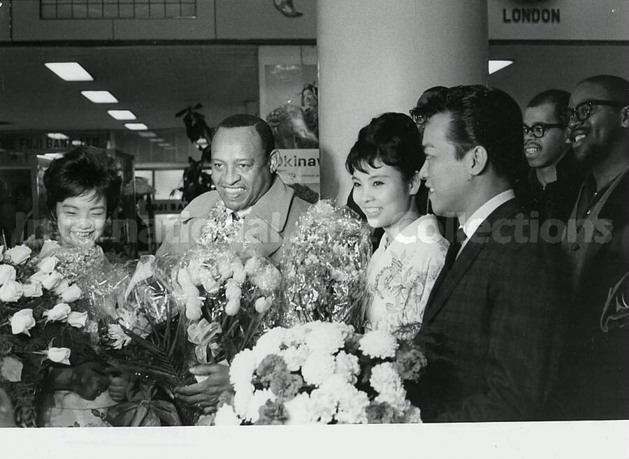 4 1/2 x 6 1/2 inch photograph. Lionel Hampton is welcomed with flowers in an airport terminal [in Japan]