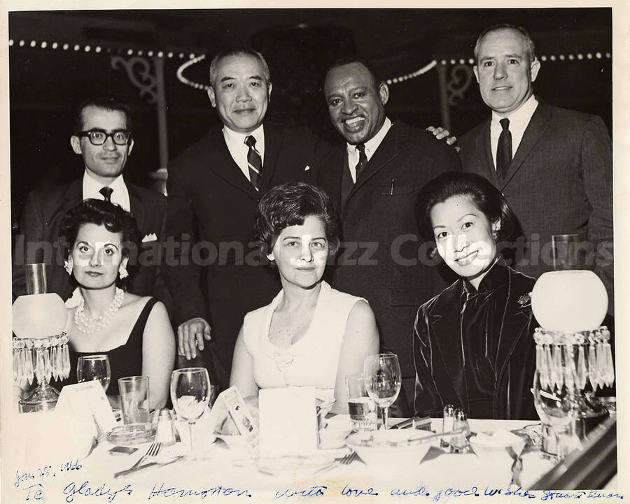 8 x 10 inch photograph. Lionel Hampton with unidentified persons. Place cards on the dinner table reads: Riverboat; Rise to the occasion. This photograph is dedicated to Gladys Hampton