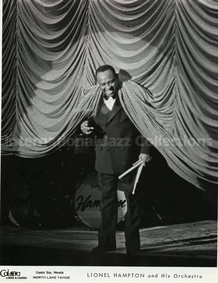 10 x 8 inch promotional photograph. Lionel Hampton poses under the stage curtain, holding drumsticks