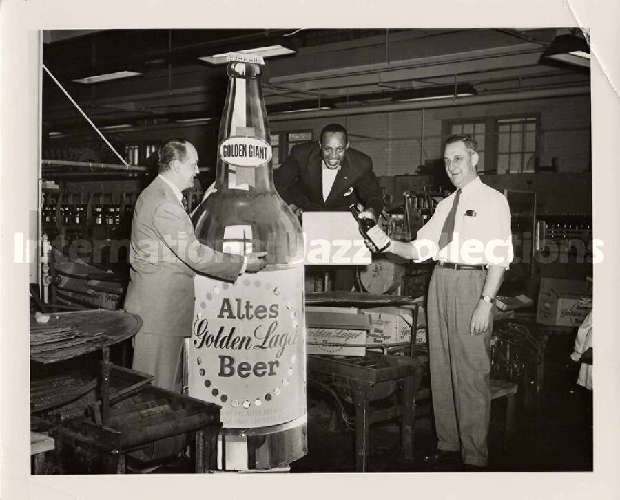 8 x 10 inch photograph. Lionel Hampton at the Altes Brewery. Handwritten on the back of the photograph: left to right-Arthur Wible, Altes vice-president; Lionel Hampton; August Quandt, vice-president and plant supervisor. Picture was taken as first Golden Giants came off bottling line of Altes Brewery