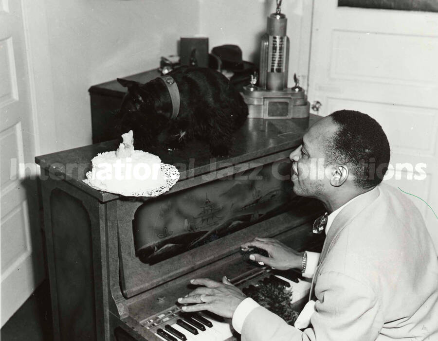 8 x 10 inch photograph. Lionel Hampton playing the piano with his dog. A note accompanying the photograph reads: Birthday Note. Hollywood. Lionel Hampton, well known swing band leader, plays 'Tempo's Birthday' in honor of his Scottie Tempo who celebrated his tenth birthday recently. The cake and the new jump tune that Hampton played were birthday tributes to the dog  who has traveled everywhere with his owner and his band for the last decade