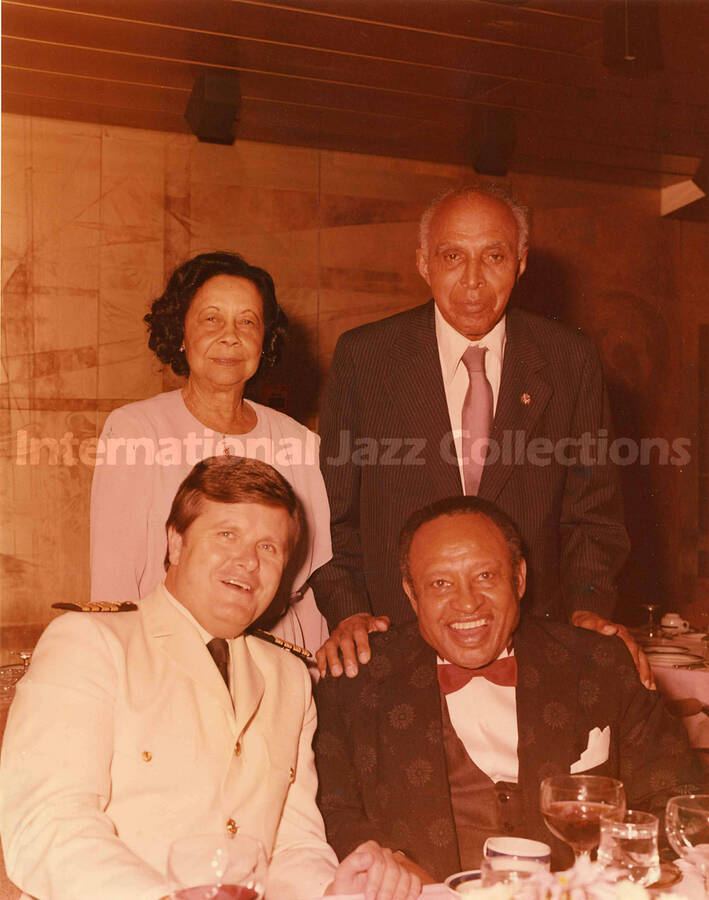 10 x 8 inch photograph. Lionel Hampton seated on the right, poses with three unidentified persons