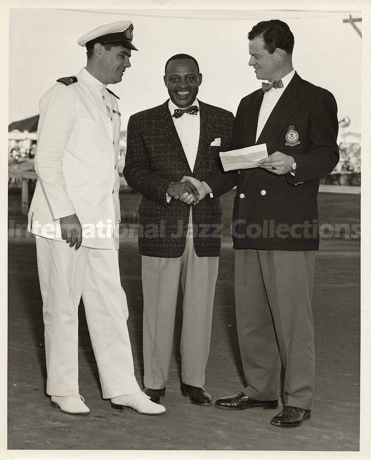 10 x 8 inch photograph. Lionel Hampton with unidentified [Royal Navy Officer?] and a man wearing a jacket with a badge of the [Royal Air Force?]