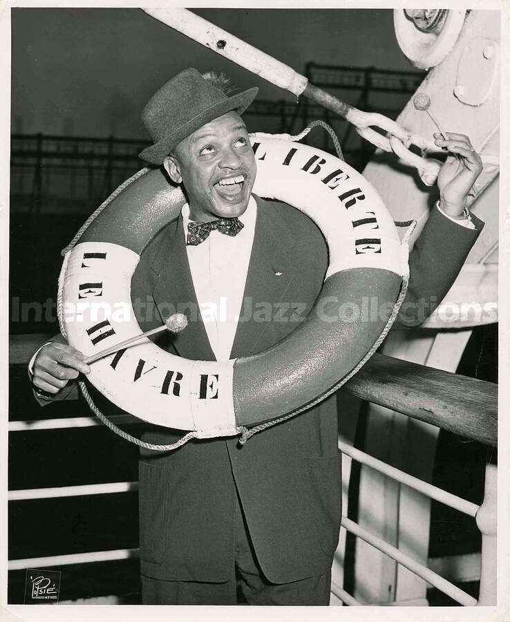10 x 8 inch photograph. Lionel Hampton poses on board of a ship, with a life preserver ring bearing  inscriptions in French: Liberte; Le Havre. This photograph was probably taken on his return to the United States after a tour in Europe