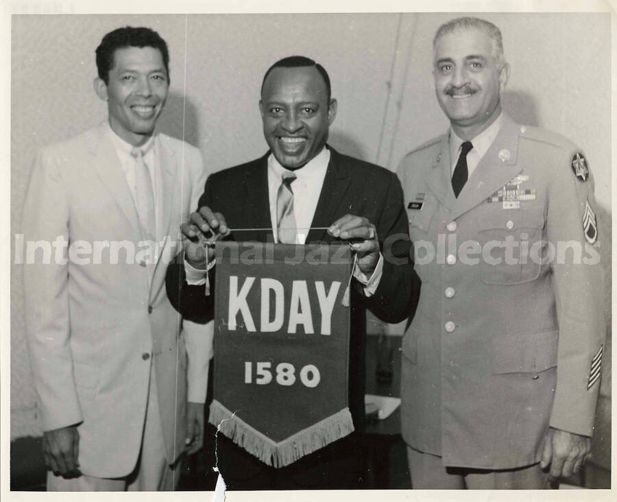8 x 10 inch photograph. Lionel Hampton holding a banner of the radio station KDAY 1580 with two unidentified men
