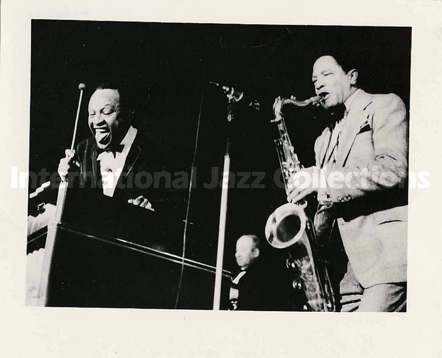 4 1/2 x 5 1/4 inch photograph. Lionel Hampton playing the vibraphone with Illinois Jacquet playing the saxophone. In the background is guitarist Billy Mackel