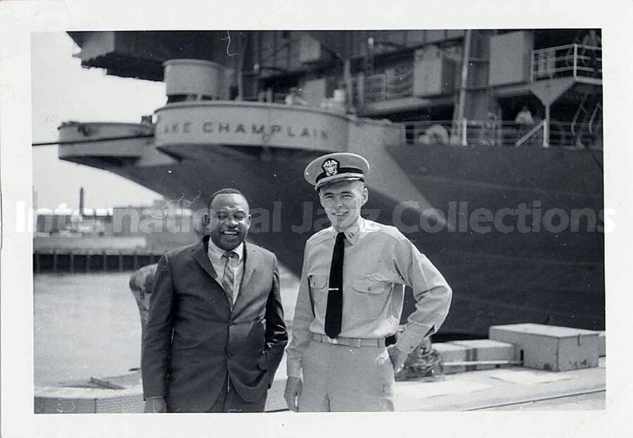 3 1/2 x 5 inch photograph. Lionel Hampton with unidentified military person; The ship USS Lake Champlain CV-39 is in the background