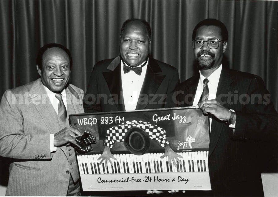 5 x 7 inch photograph. Lionel Hampton and two unidentified men hold a picture that says: WBGO 88.3 FM - Great Jazz - Jazz 88 -Commercial-Free 24 Hours a Day