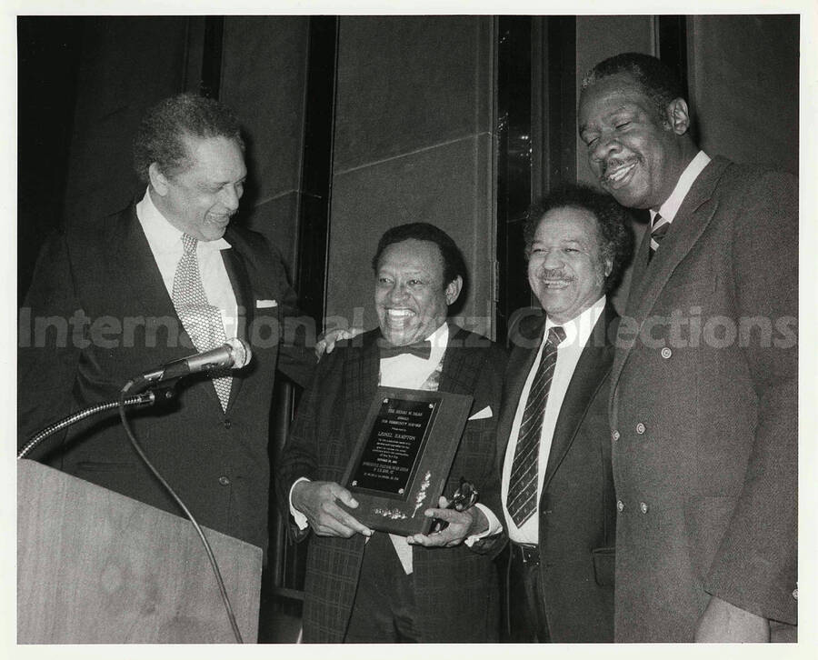 8 x 10 inch photograph. Lionel Hampton receiving the Henri M. Deas Award for Community Service presented by the Opportunities Industrialization Center of New York. Milton A. Galamison is on Lionel Hampton's left side