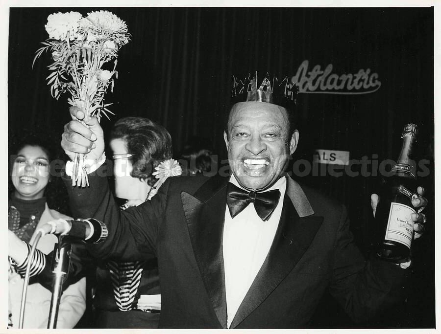 7 x 9 1/2 inch photograph. Lionel Hampton wearing a paper crown holds a bottle of Veuve Clicquot champagne - Gout Americain. Seen in the background is the word: Atlantic