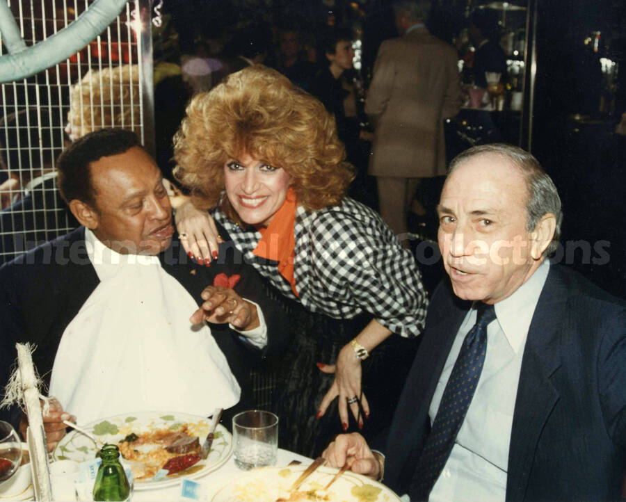 8 x 10 inch photograph. Lionel Hampton with Sylvia Bennett and an unidentified man in a restaurant