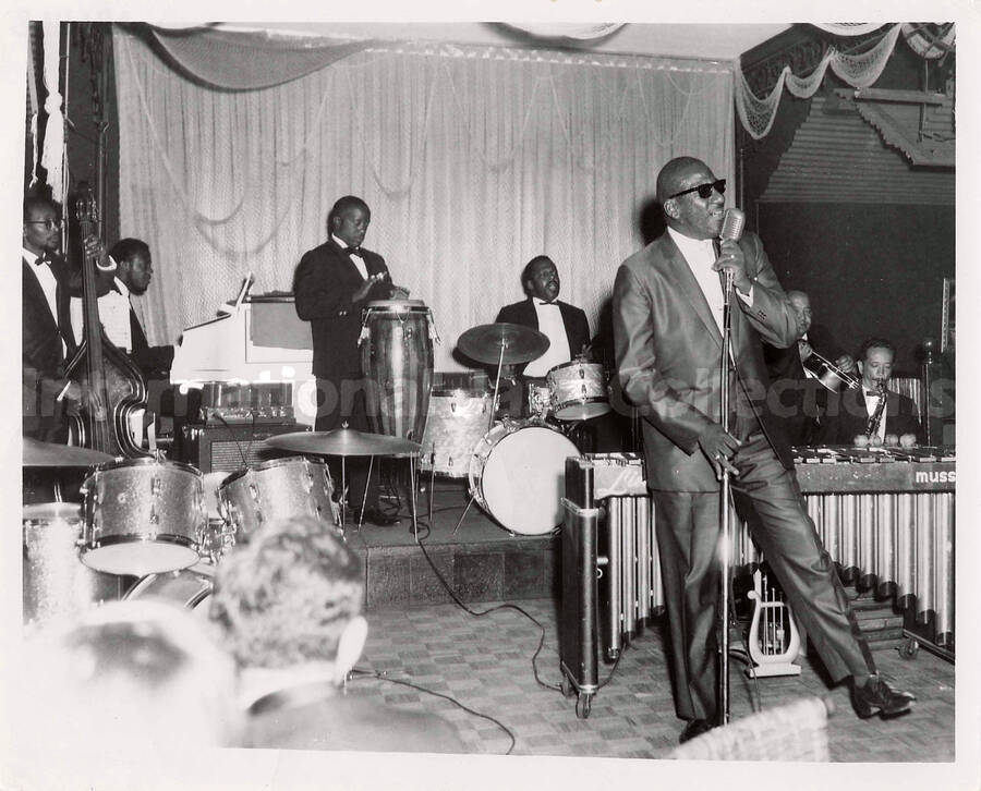 8 x 10 inch photograph. Unidentified vocalist performing with Lionel Hampton's band, which includes guitarist Billy Mackel