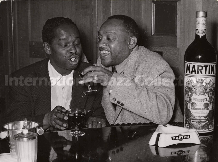 7 x 9 1/2 inch photograph. Lionel Hampton drinks Martini vermouth with unidentified man, in Brussels, Belgium