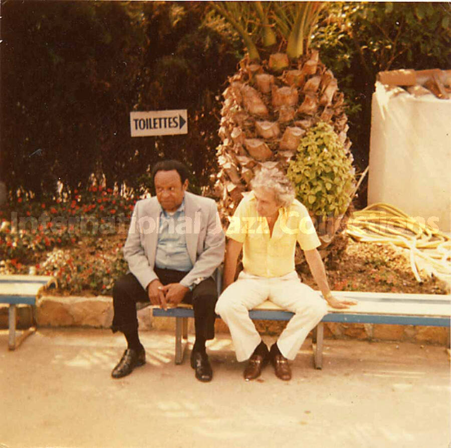 3 1/2 x 3 1/2 inch photograph. Lionel Hampton and Bill Titone rest on a bench at a marine mammal park