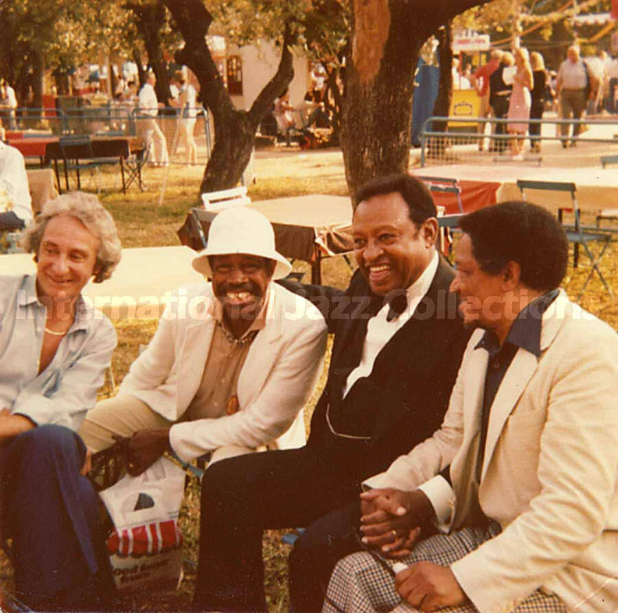3 1/2 x 3 1/2 inch photograph. Bill Titone, Al Grey, Lionel Hampton, and an unidentified man sitting on a bench in a park
