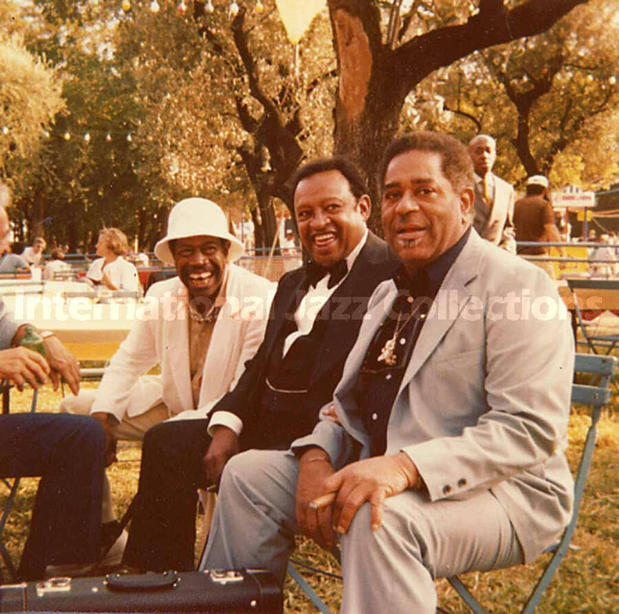 3 1/2 x 3 1/2 inch photograph. Al Grey, Lionel Hampton, and Dizzy Gillespie sitting on a bench in a park