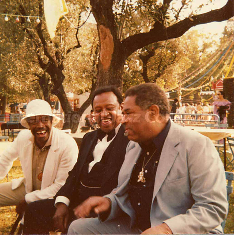 3 1/2 x 3 1/2 inch photograph. Al Grey, Lionel Hampton, and Dizzy Gillespie sitting on a bench in a park