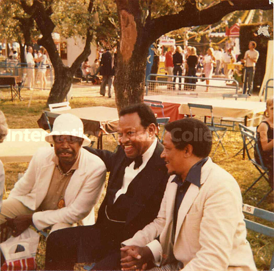 3 1/2 x 3 1/2 inch photograph. Al Grey, Lionel Hampton, and an unidentified man sitting on a bench in a park