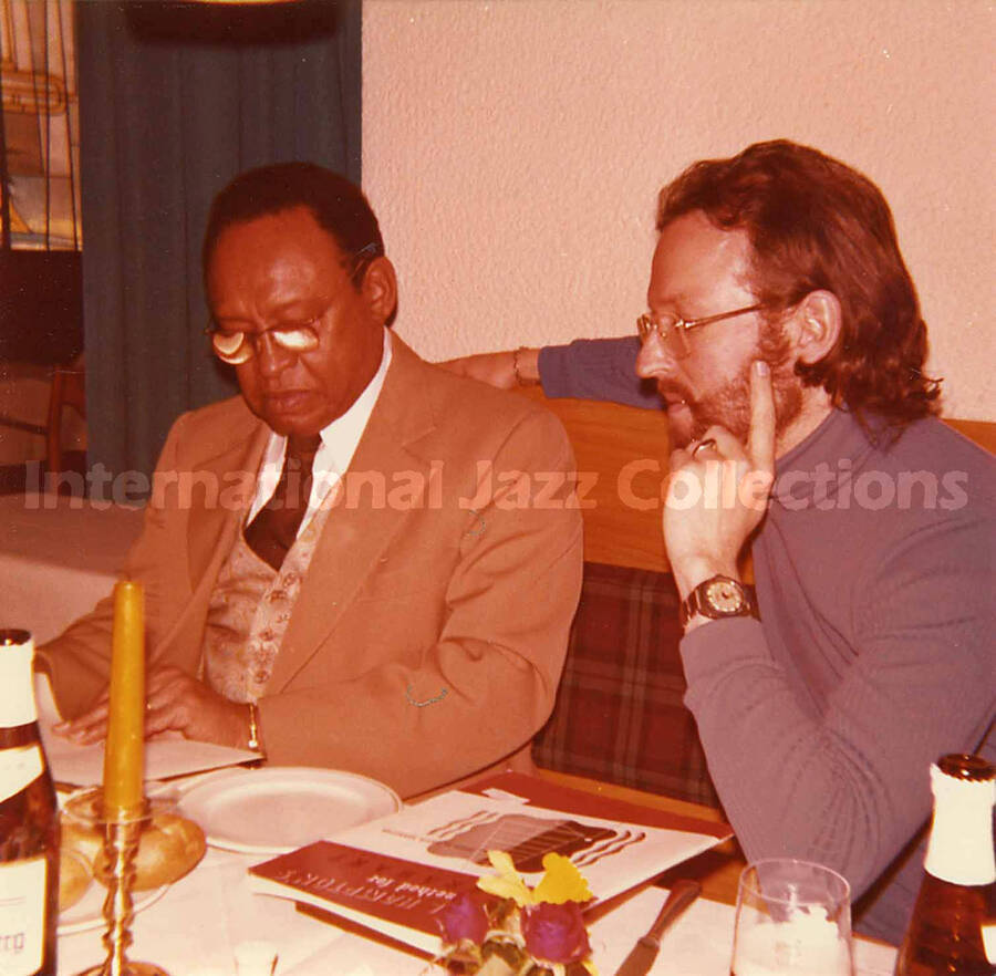 5 x 5 inch photograph. Lionel Hampton and Jean Claude Forestier in a restaurant. Seen on the table is a copy of the book: Lionel Hampton's Method for Vibraharp